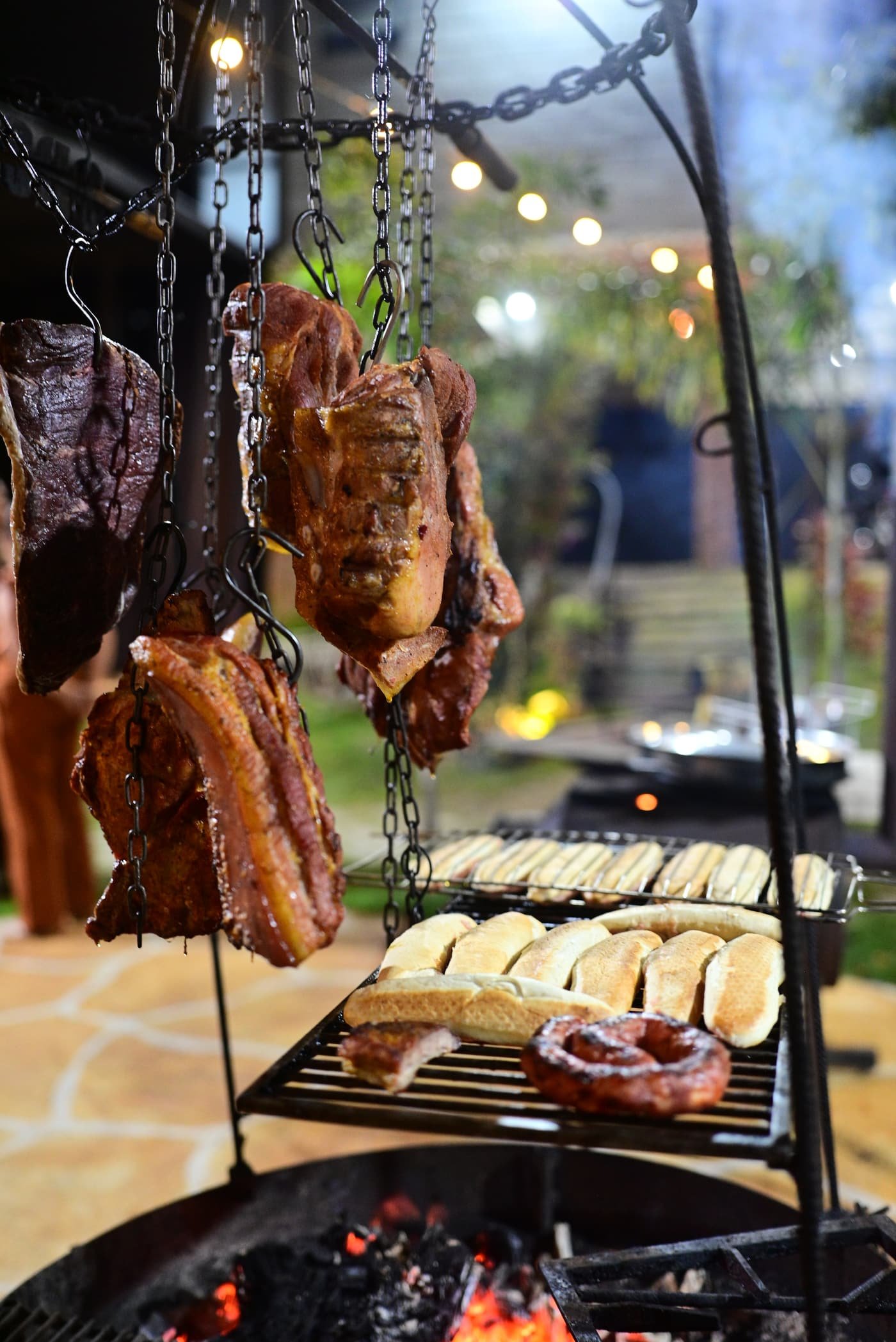 Carnes e linguiças assando com luzes de varal ao fundo